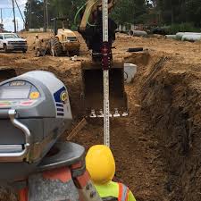 Person in high-visibility vest and hard hat working on a construction site with excavation equipment. Using spectra pipe laser 