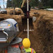 Person in high-visibility vest and hard hat working on a construction site with excavation equipment. Using spectra pipe laser 